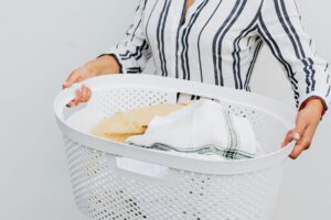 A close-up of a woman holding a white laundry basket filled with fresh, clean clothes.